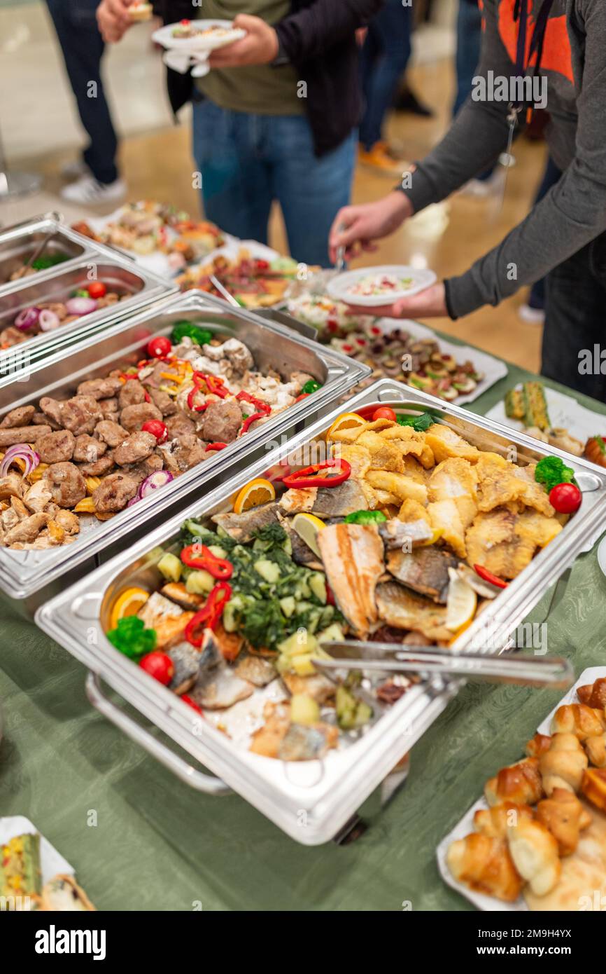 Warming dishes with food and people serving themselves. Buffet event