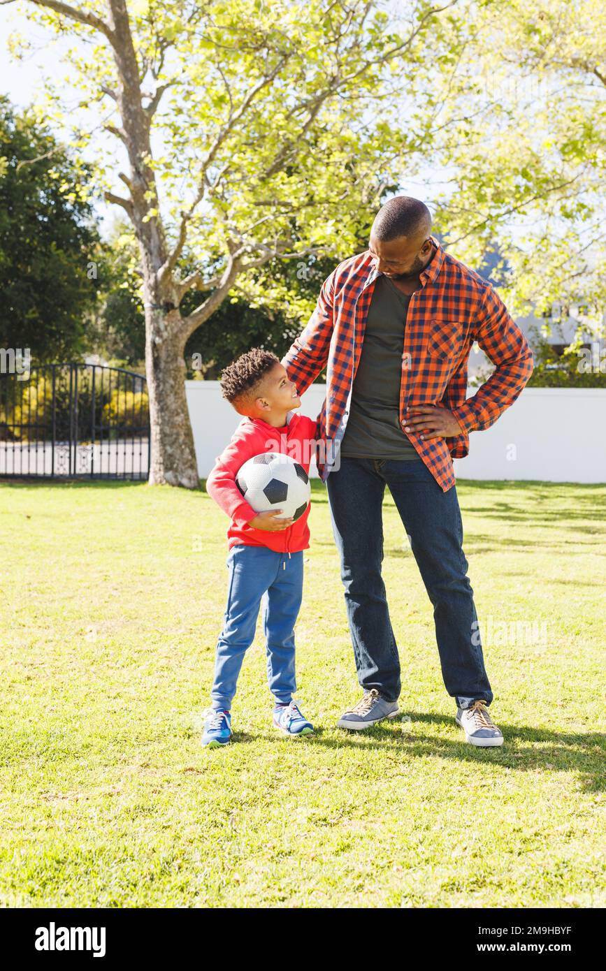 Happy african american father and son playing football in their backyard Stock Photo