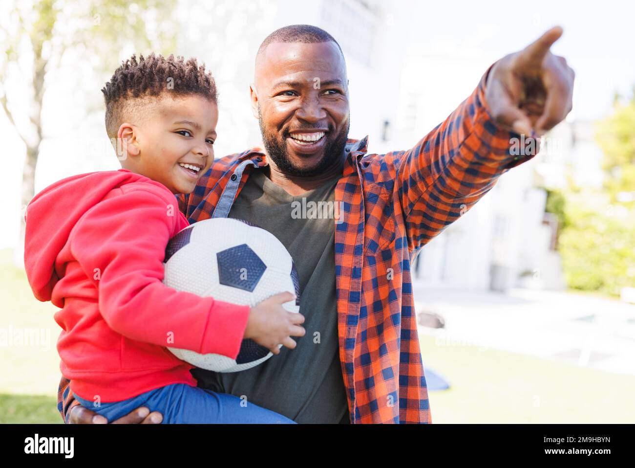 Happy african american father and son playing football in their ...