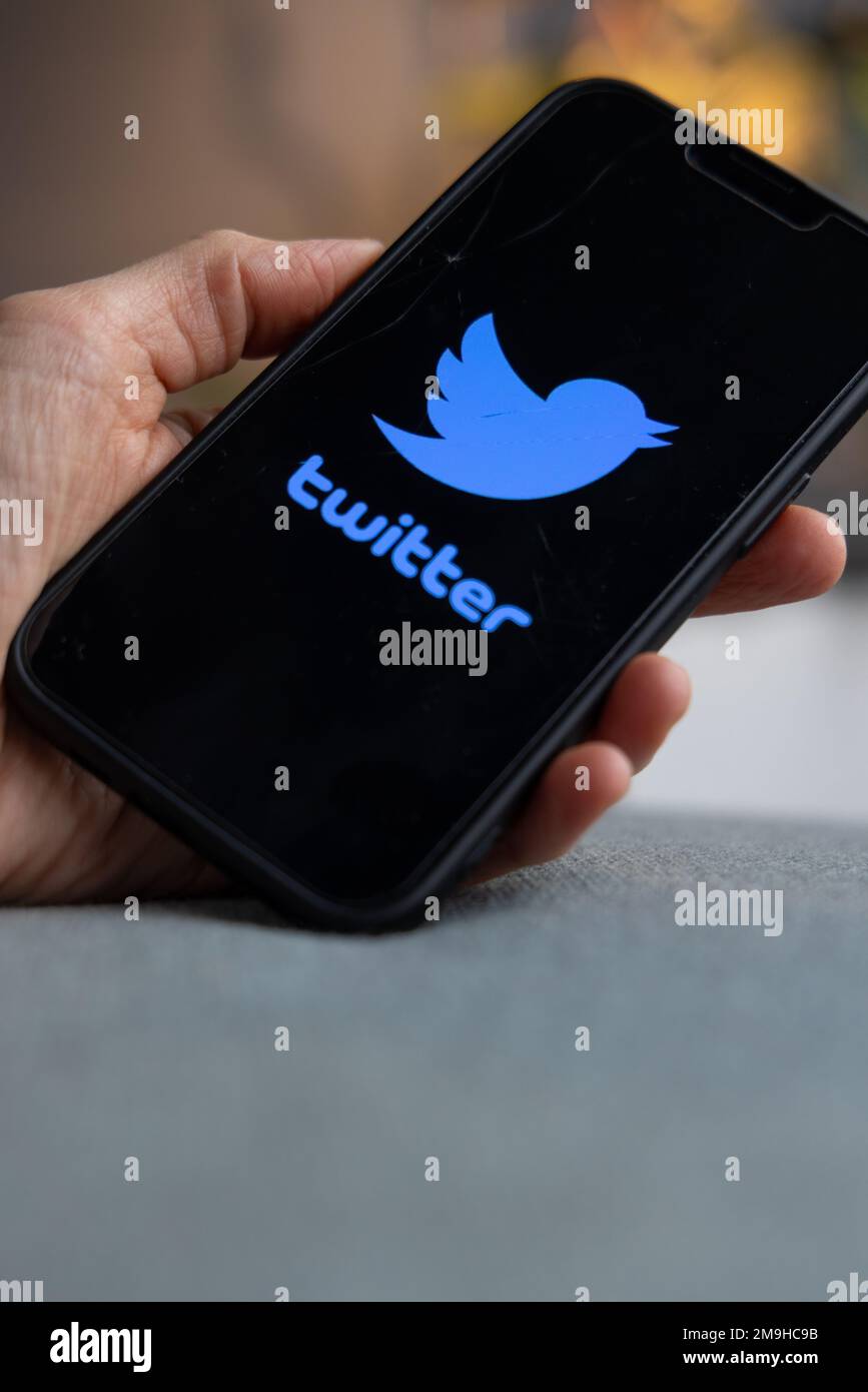 Hand holding a smartphone with Twitter icon on screen. Blue bird and word Twitter on black screen. IPhone with a social media app logo. Amsterdam, Net Stock Photo