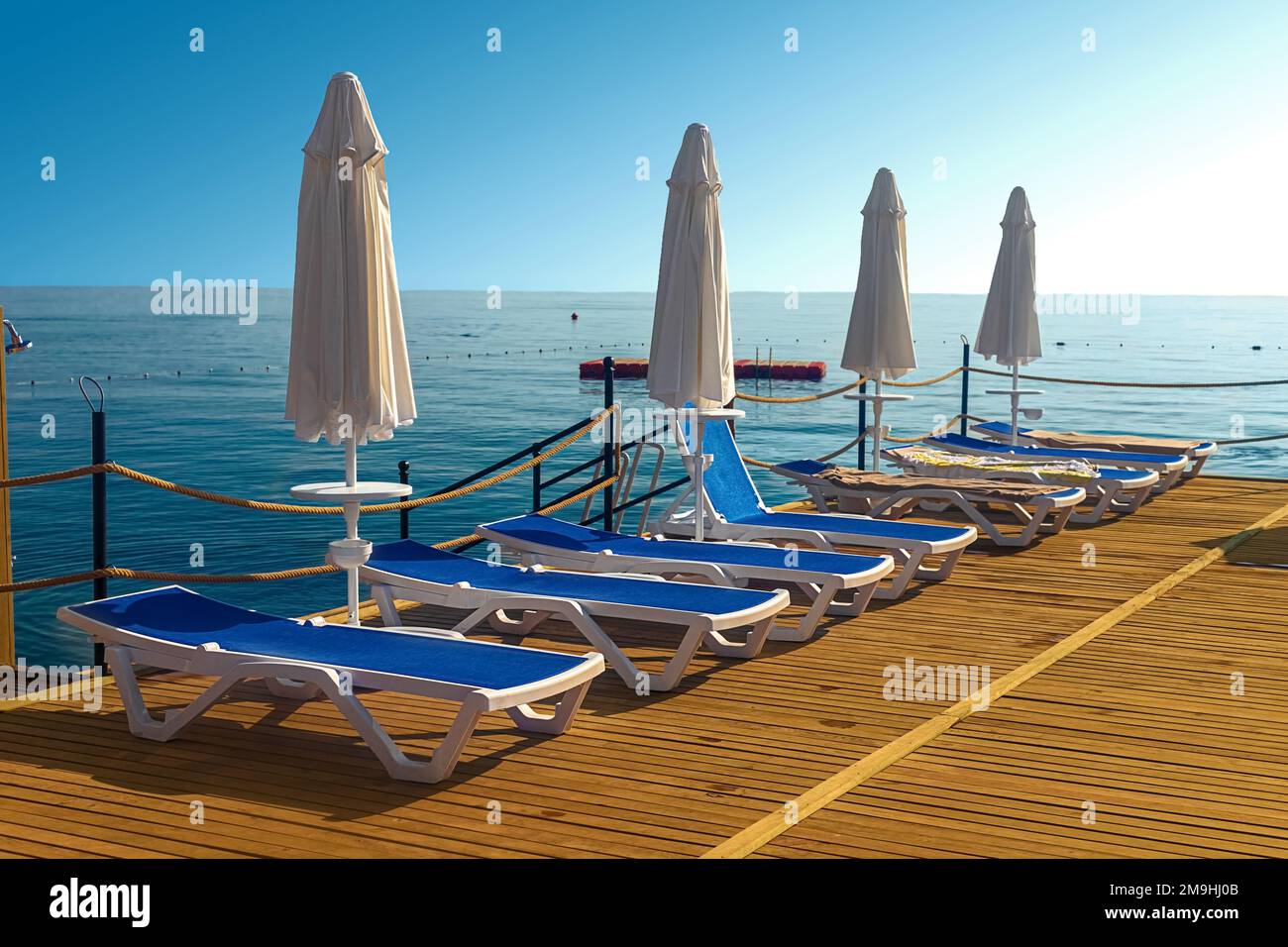 View of the pier with blue sun loungers and white umbrellas on the seashore in Kemer. Turkey Stock Photo