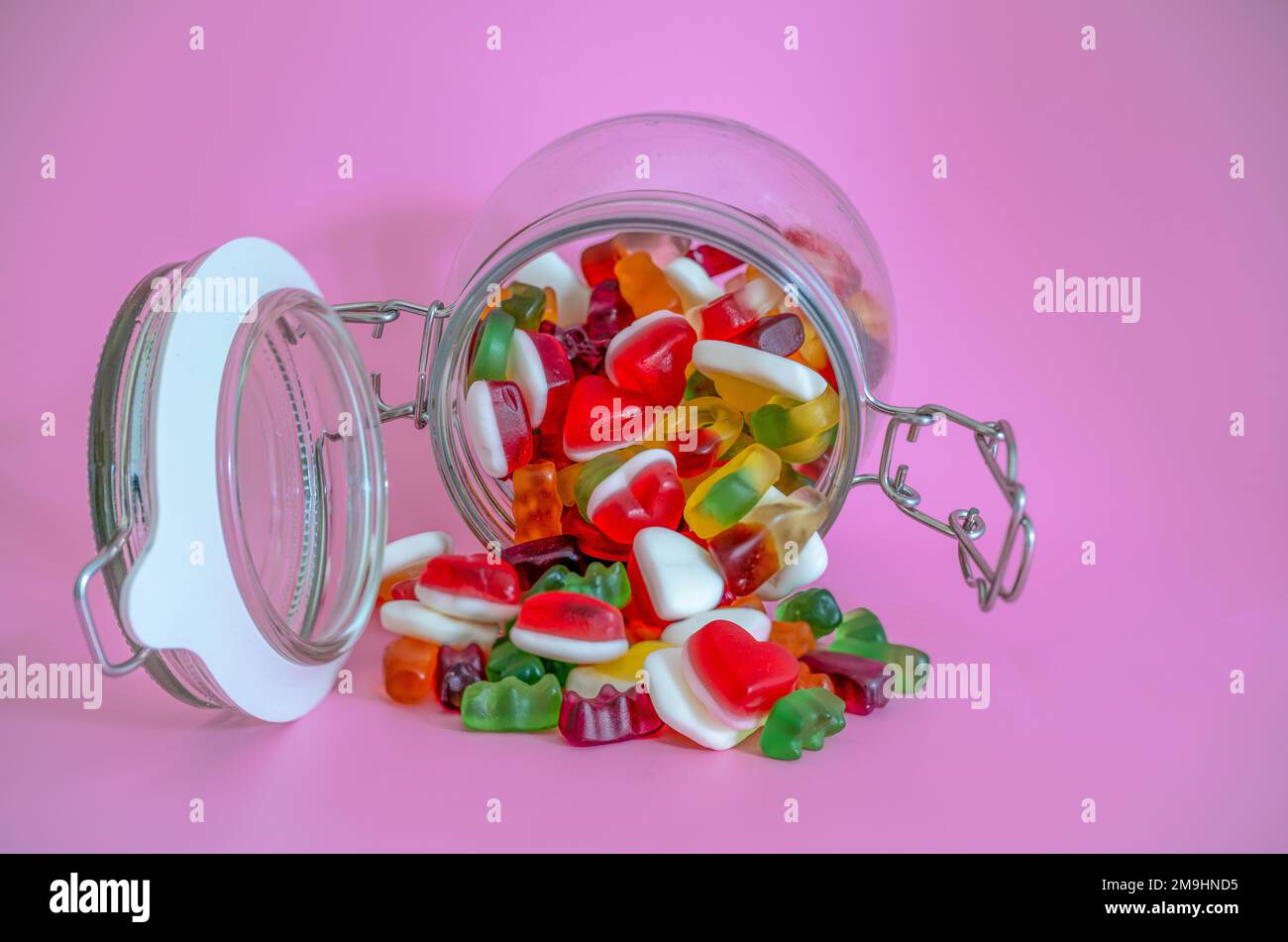 open air tight candy jar with contents spilling out onto pink