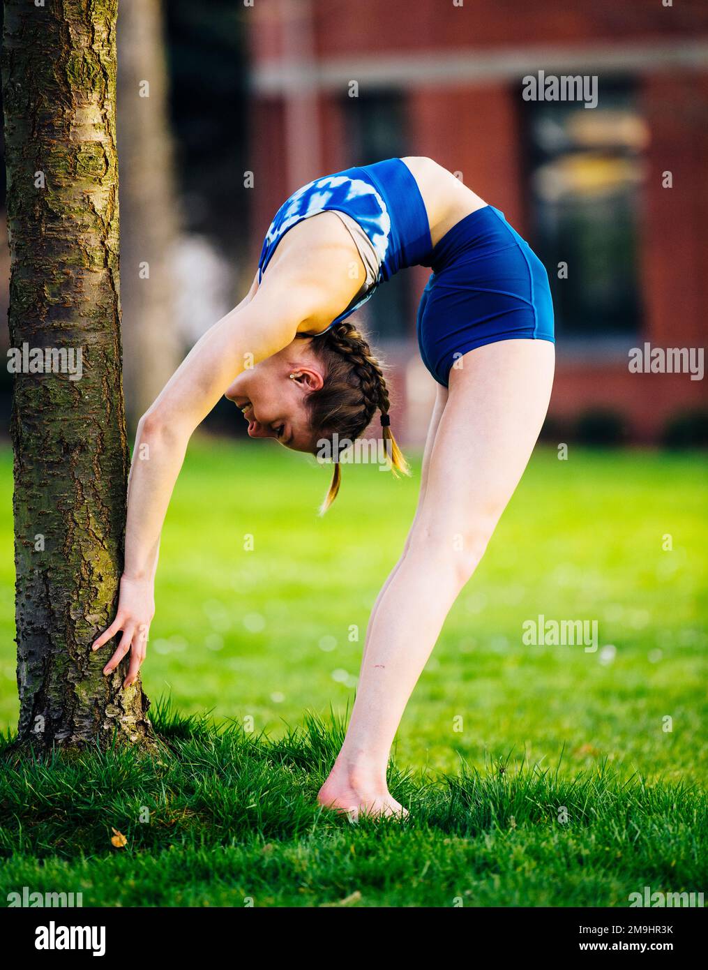Acrobat in blue clothing stretching under tree in park, University of ...