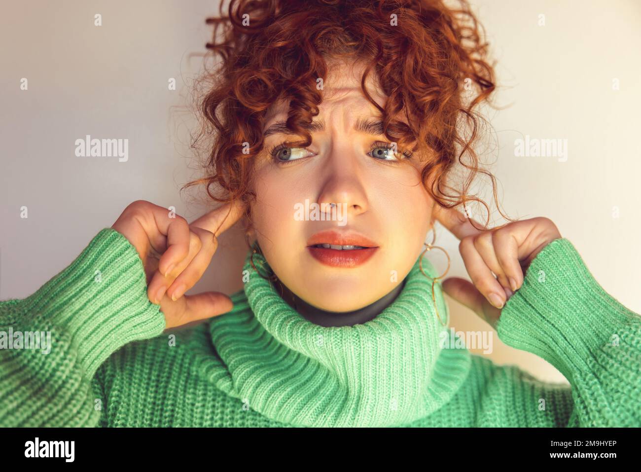 Headshot of a ginger girl looking stressed and closing her ears Stock