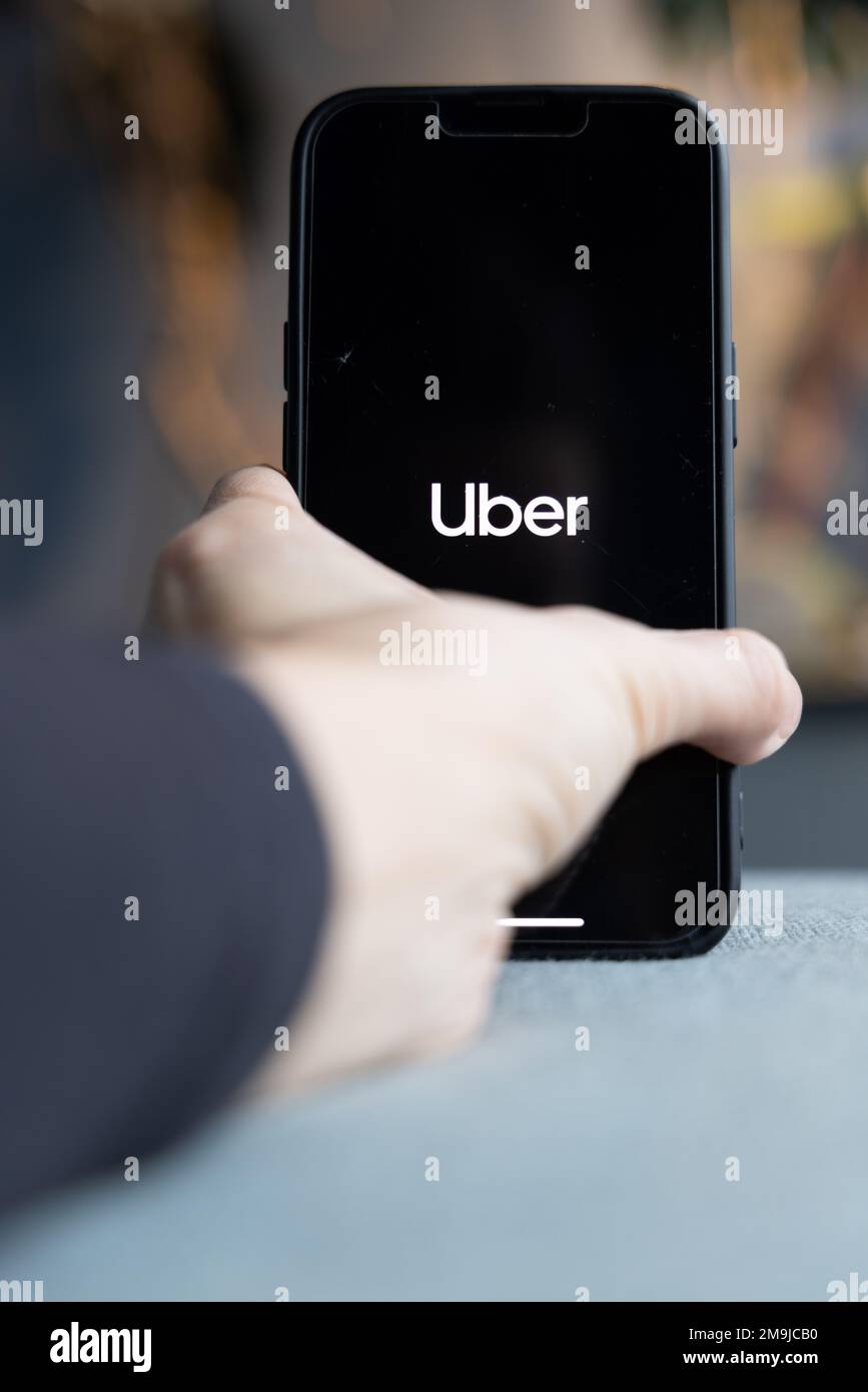Hand holding a smartphone with Uber icon on screen. White Uber on black screen. IPhone with a transportation app logo. Amsterdam, Netherlands 2023.01. Stock Photo