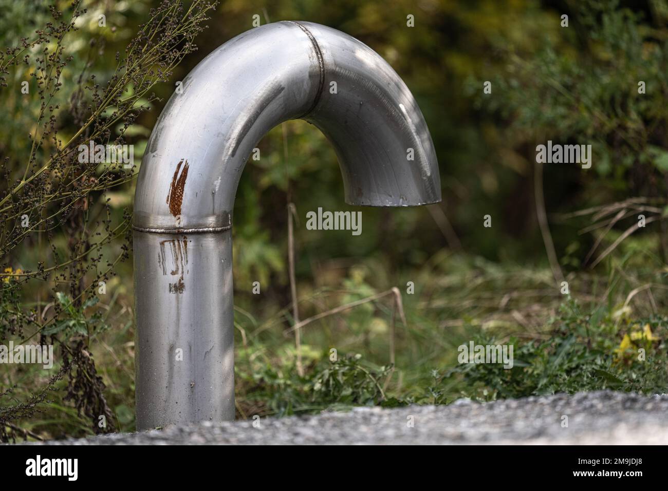 A large industrial curved silver pipe in a park Stock Photo