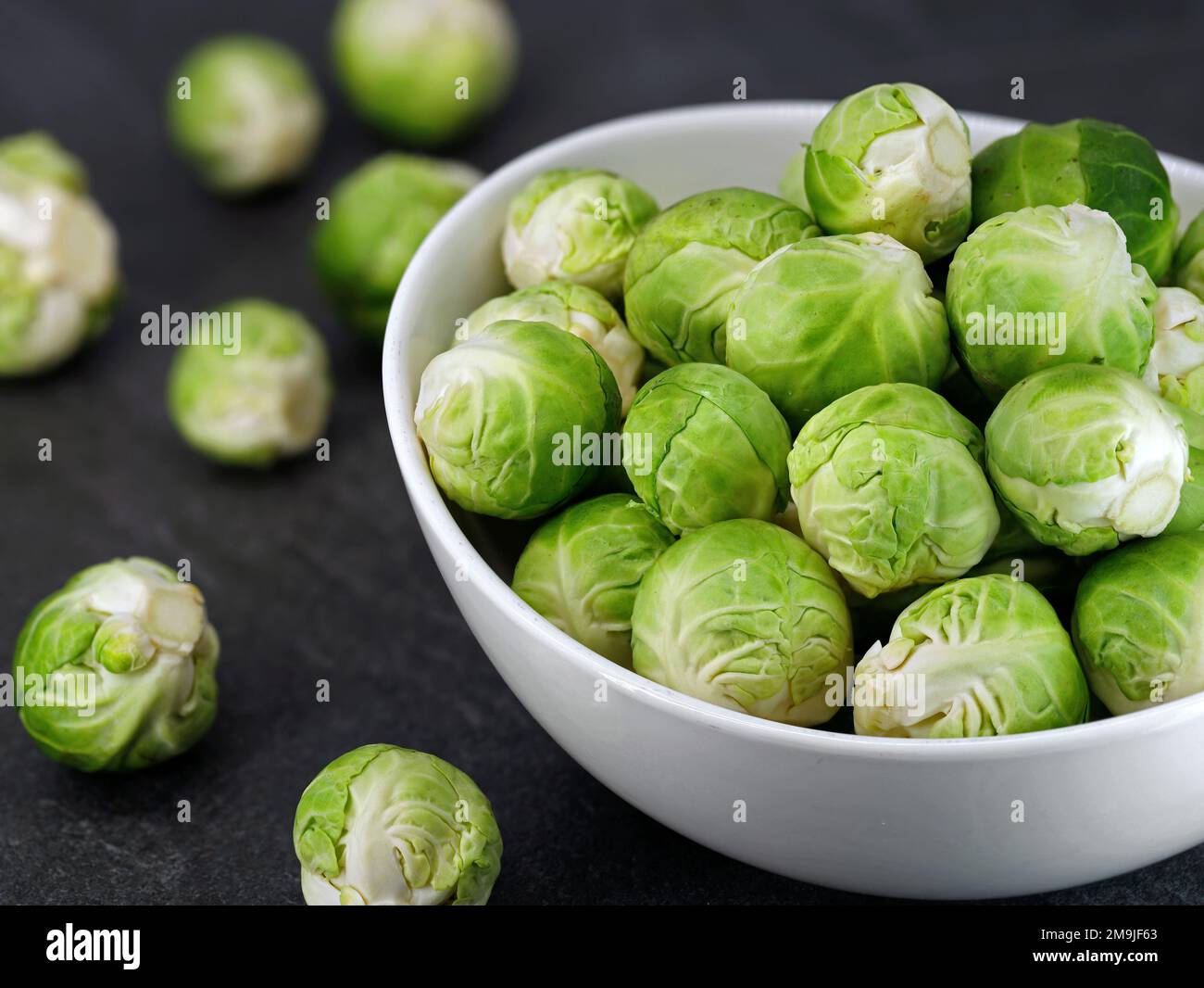 Close up of organic brussel sprouts in a white bowl on black stone background Stock Photo