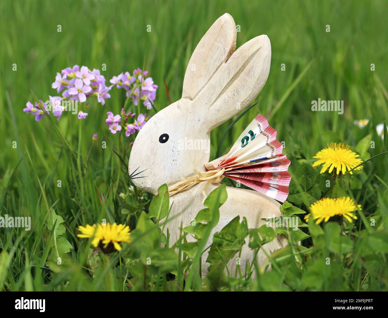 wooden easter bunny with euro banknote in green spring meadow between flowers, money gifts at easter concept image Stock Photo