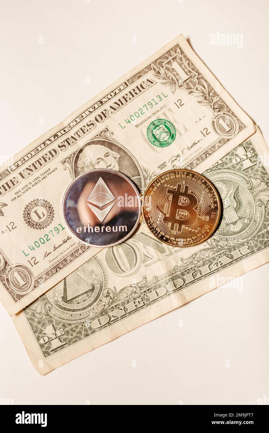 A vertical shot of an Ethereum and Bitcoin lying on two one-dollar bills on  a white background Stock Photo - Alamy