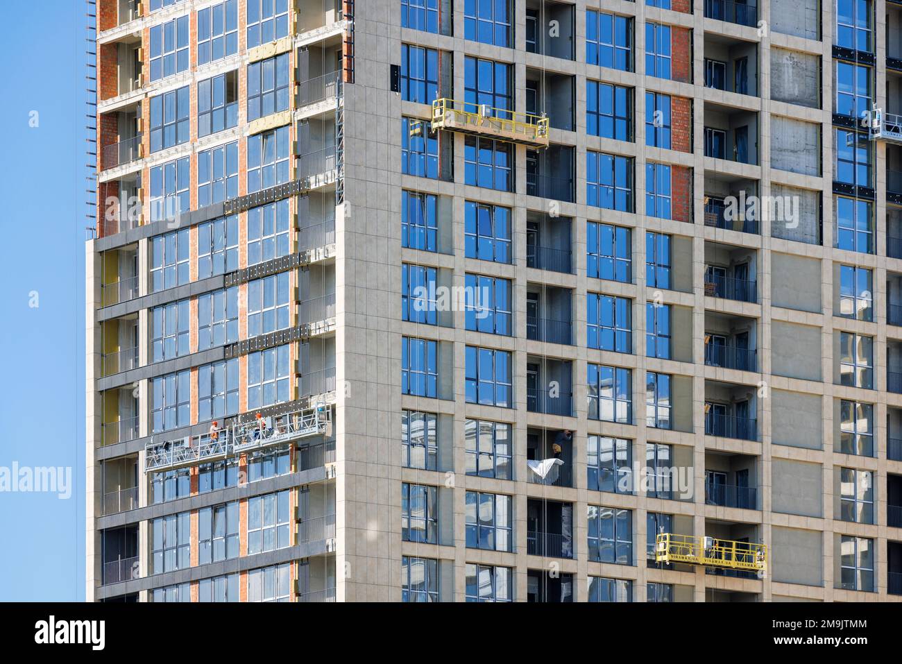 The construction of a multi-storey residential building, the work team on construction cradles makes the finishing decorative cladding of the facade. Stock Photo