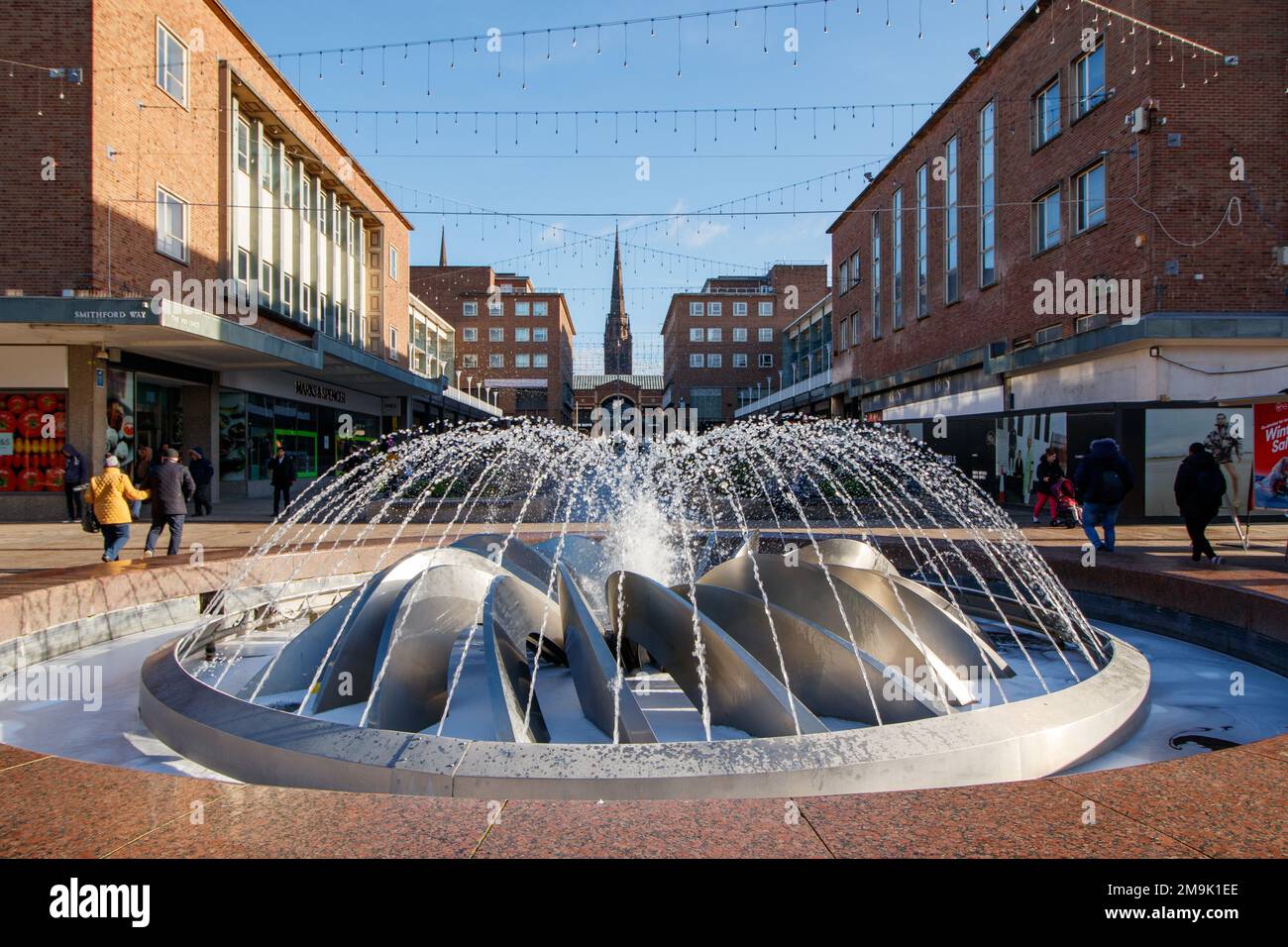 The fountain centrepiece in Smithford Way in the centre of Coventry between the upper and lower precincts. The whole area was renovated for the City of Culture 2021. The view from the fountain looks up upper precinct towards the spire of Holy Trinity Church in the distance. Stock Photo