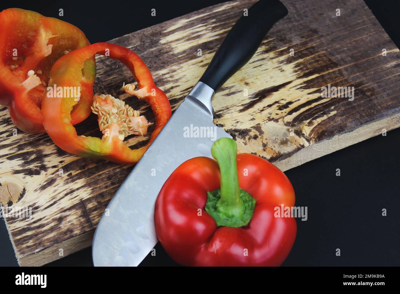 Circles of red pepper on a cutting board. High Angle View Of pepper Slices With Knife On Cutting Board On Dark Background Stock Photo