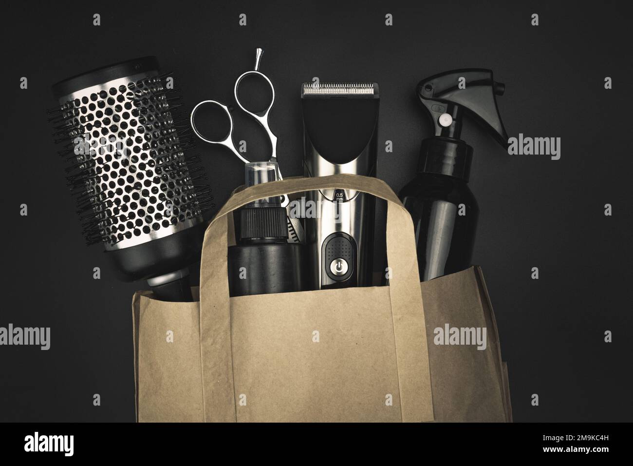 Composition with scissors, other hairdresser's accessories in a craft package on black background Stock Photo