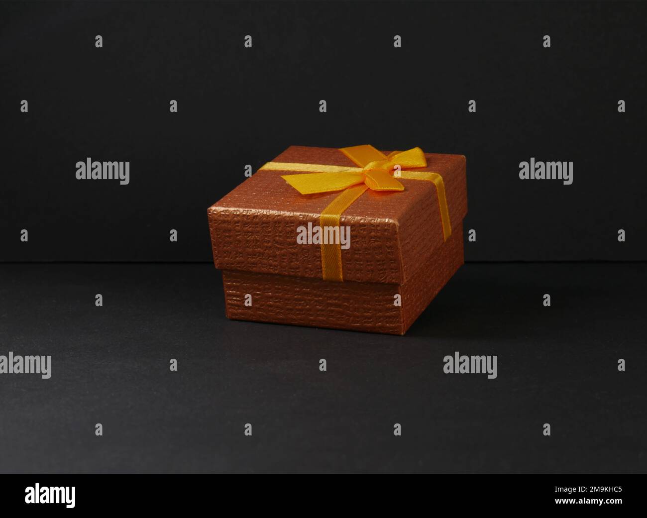 A Copper colored gift box with yellow bow on a black background. Stock Photo