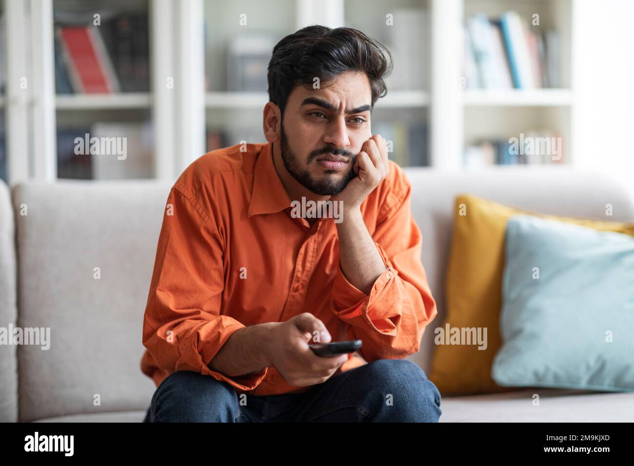 Bored middle eastern guy sitting at home, switching tv Stock Photo