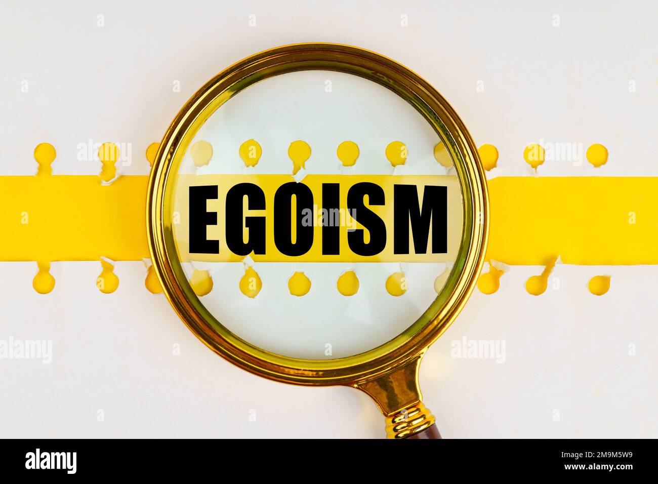 Between two sheets from a notebook on a yellow strip with the inscription - egoism, there is a magnifying glass. Stock Photo