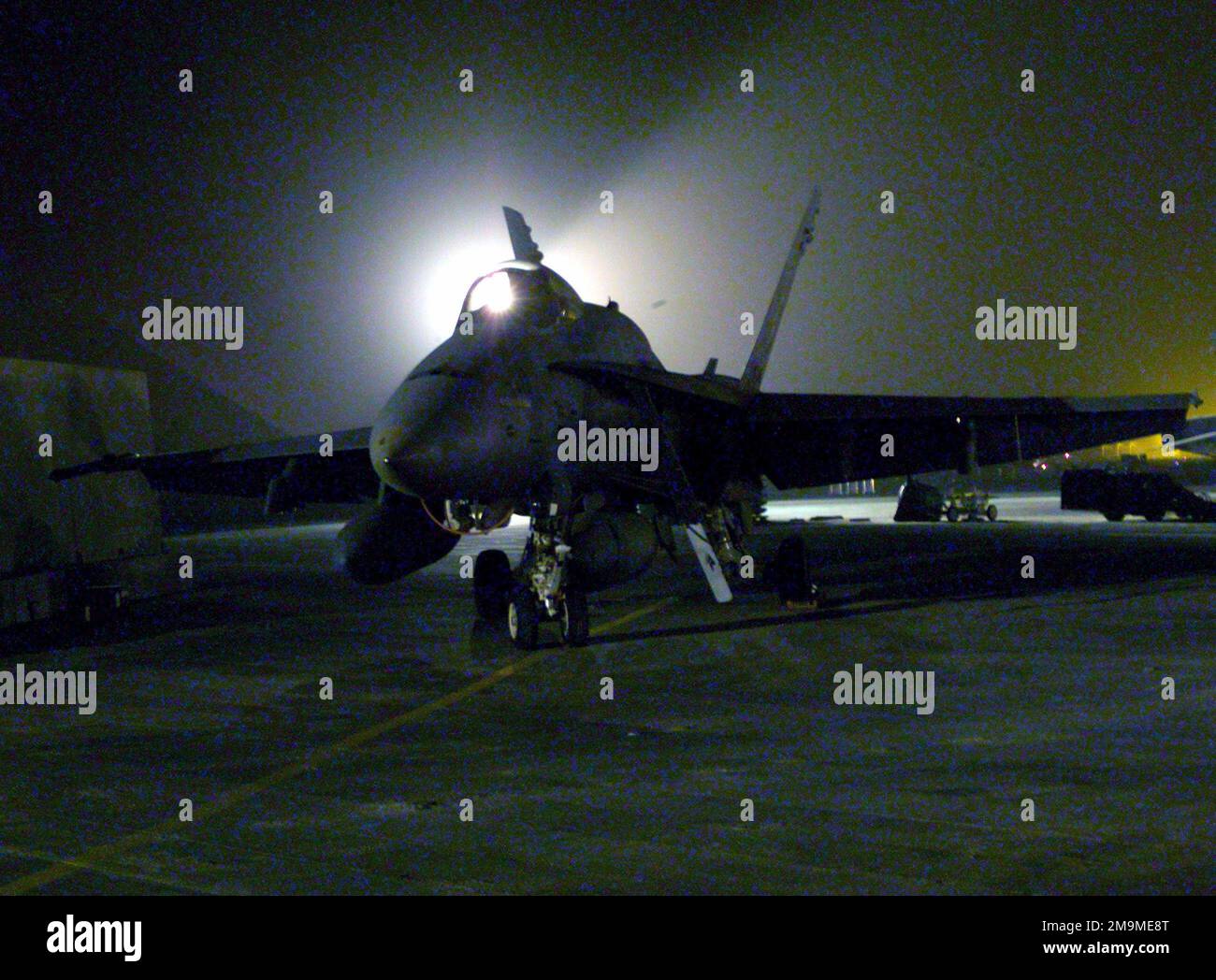 Lit at night by working lights, an F/A18D fighter sits on the