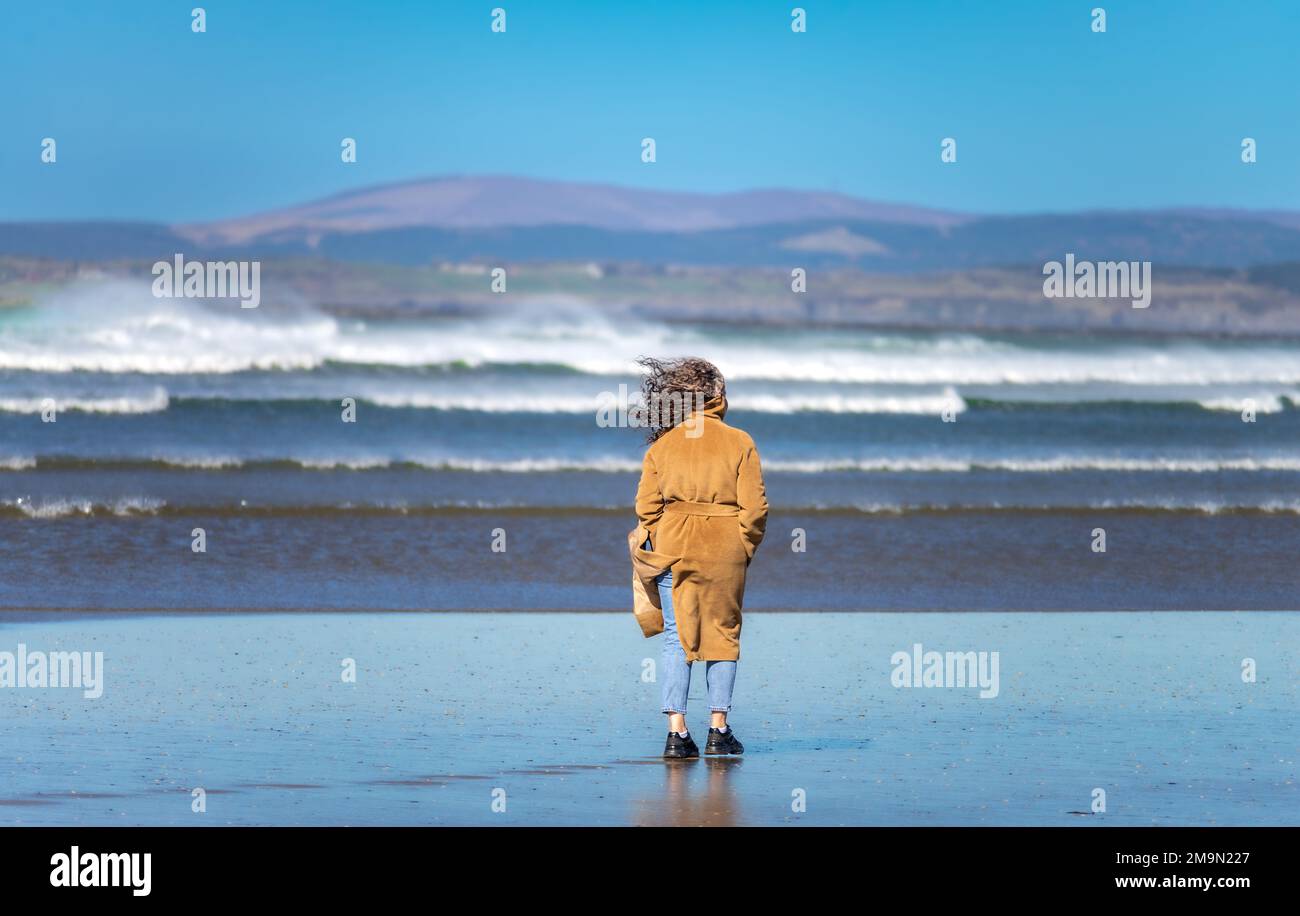 A woman walks along Rossnowlagh beach, on the windy shore of Atlantic Ocean  in the south of County Donegal in Ireland Stock Photo