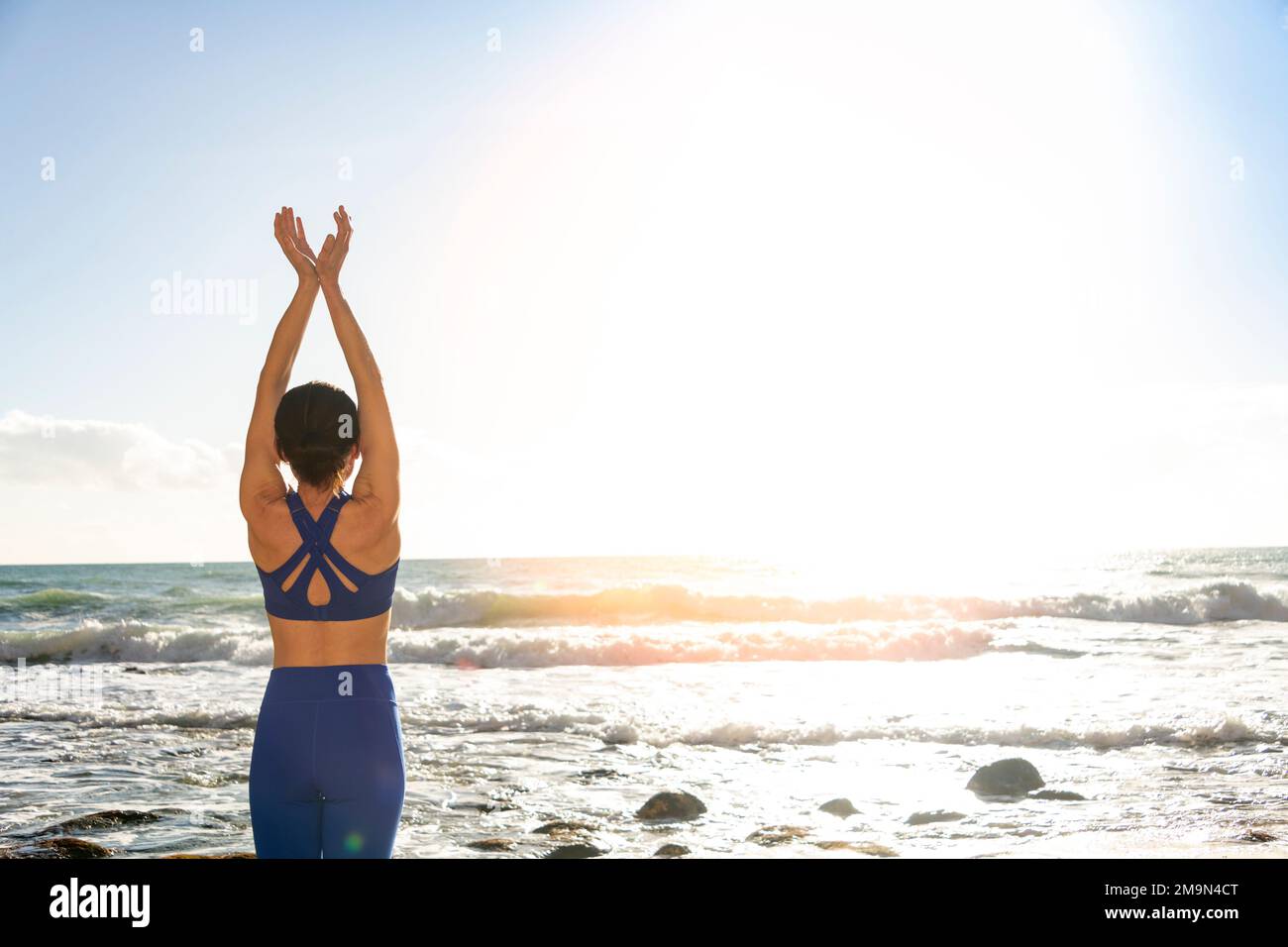 female swimmer standing on the beach doing stretching exercises Stock Photo
