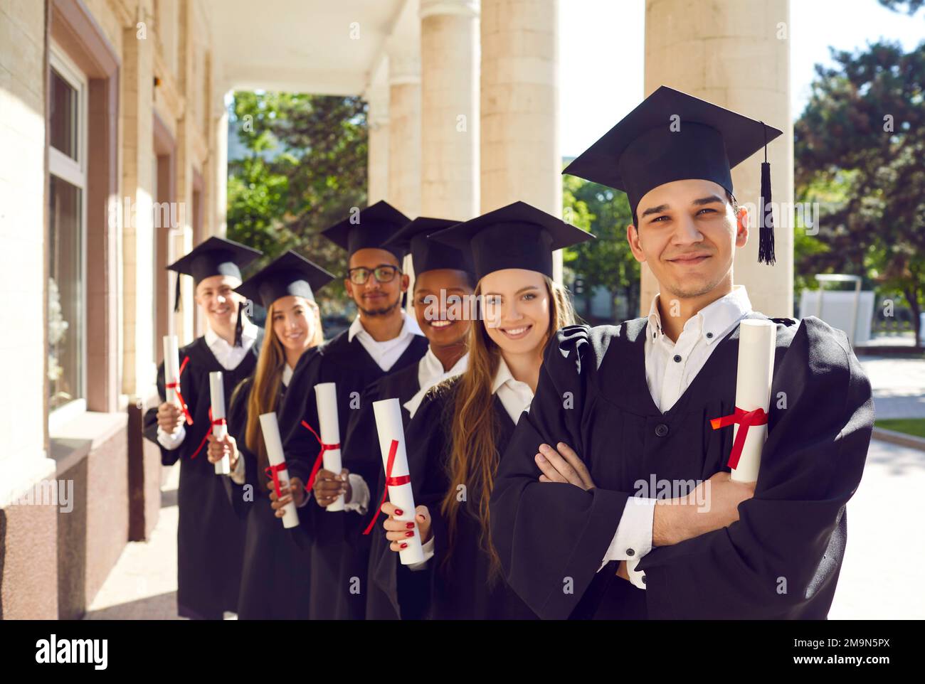 Group portrait of happy university graduates in caps and gowns holding diplomas and smiling Stock Photo