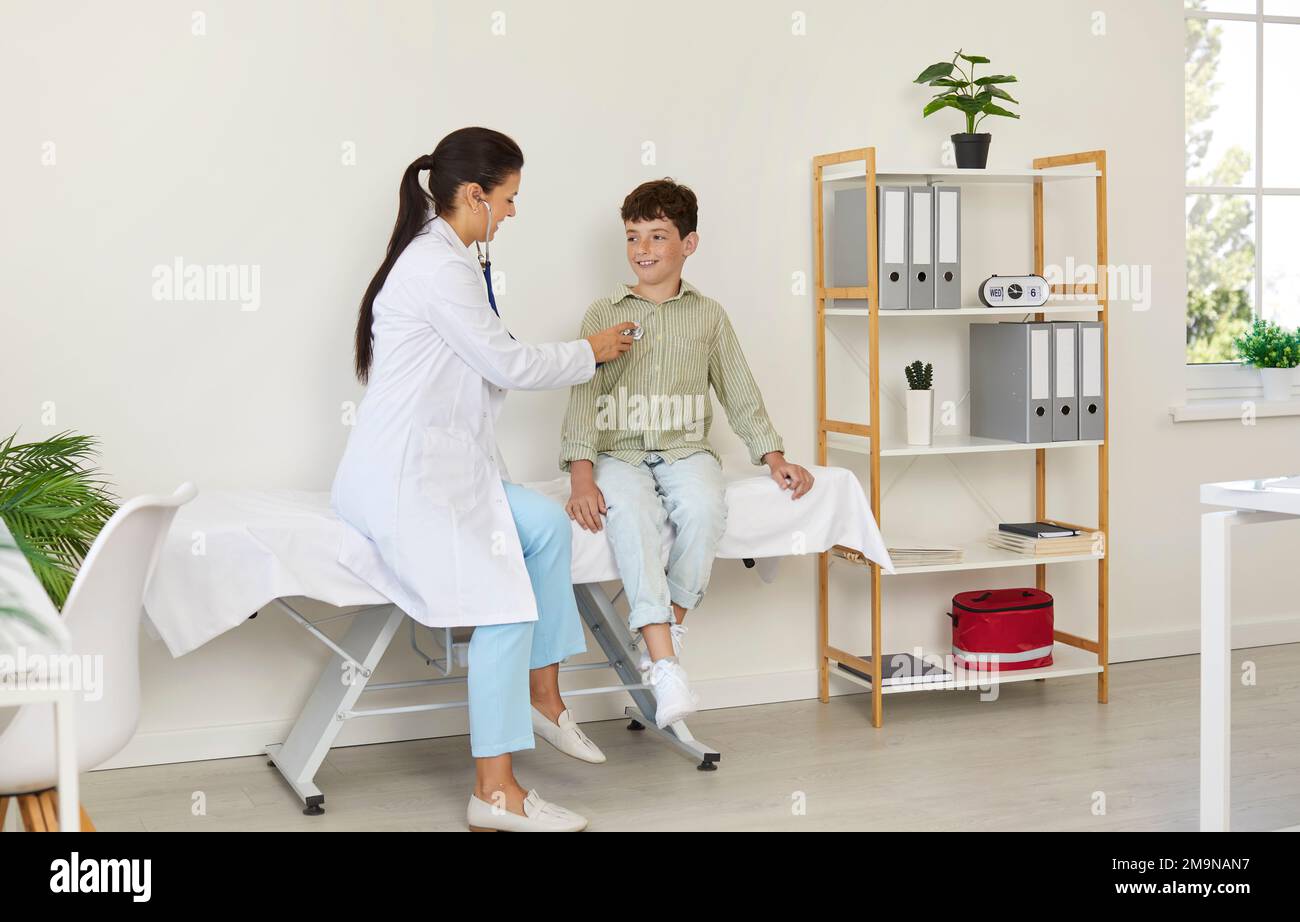 Doctor sitting on medical couch with child examining his heart or lungs
