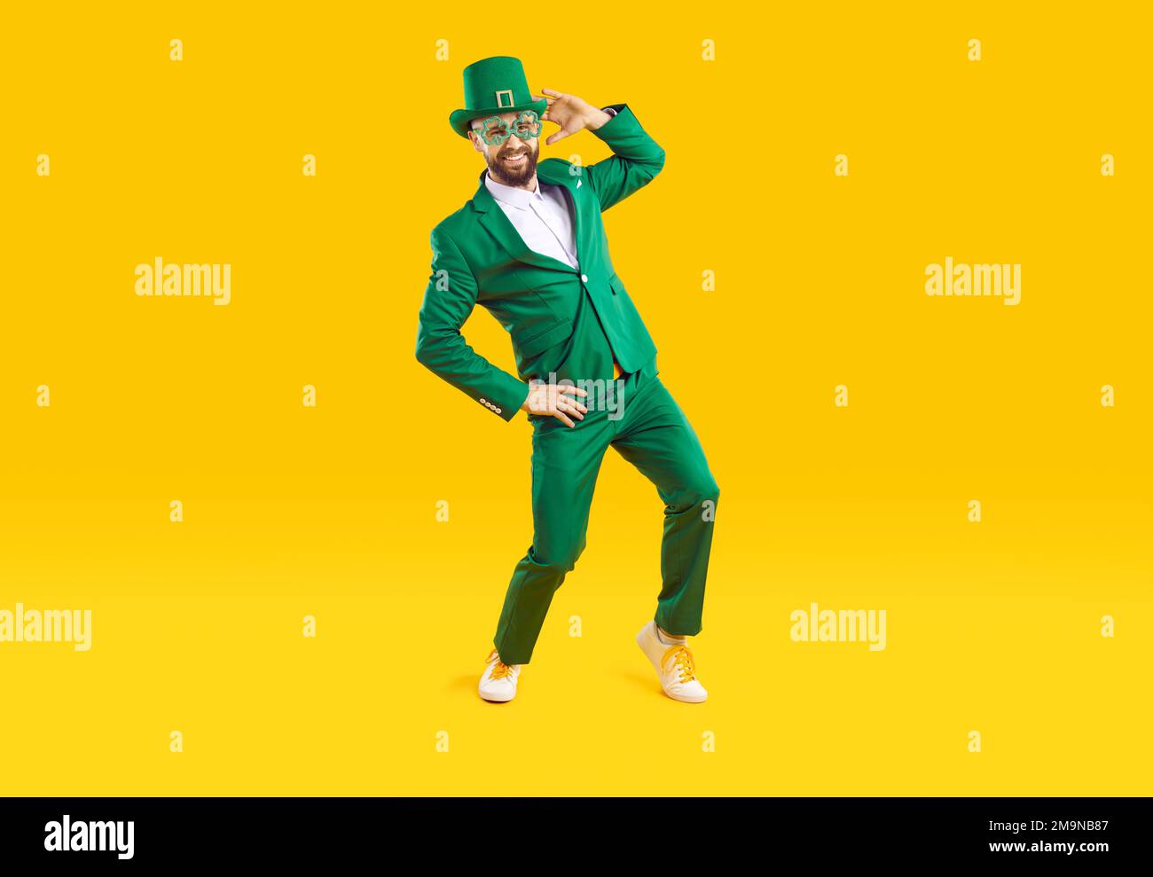 Funny stylish man in green clothes celebrates St. Patrick's Day on orange background. Stock Photo