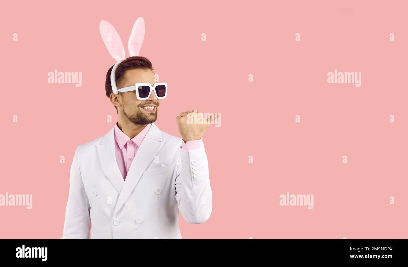 Young handsome man with easter rabbit ears and sunglasses standing over isolated pink background with happy face looking and pointing to the side Stock Photo