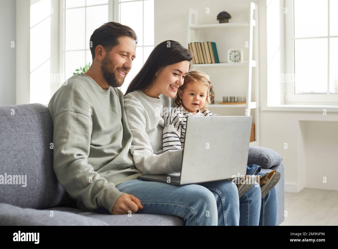 Happy family of mom, dad and cute little daughter sitting at laptop at home Stock Photo