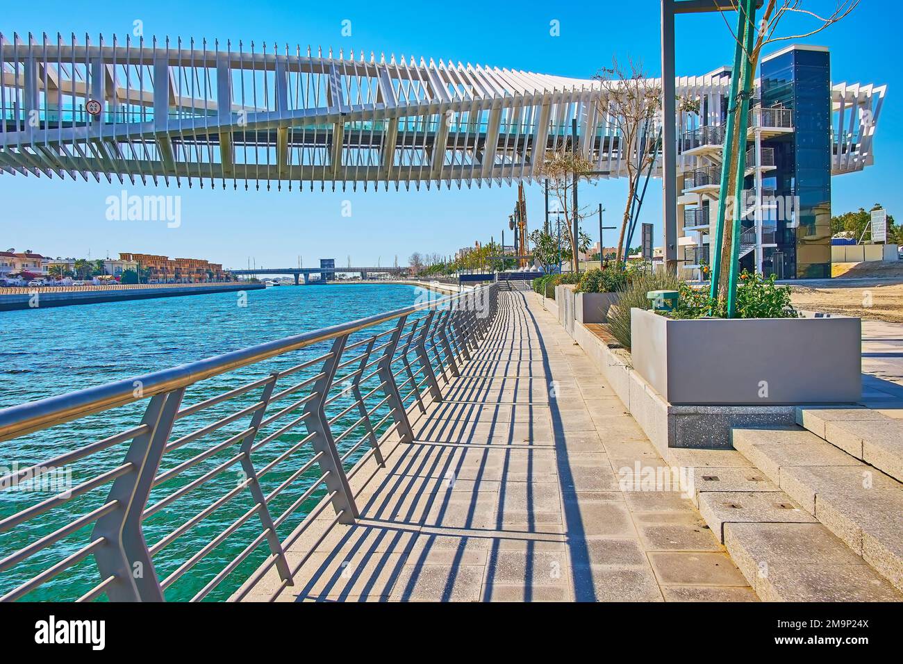 Enjoy the picturesque view of Dubai Water Canal embankment and Water Canal Footbridge (Twisted Bridge) with unusual construction, Dubai, UAE Stock Photo