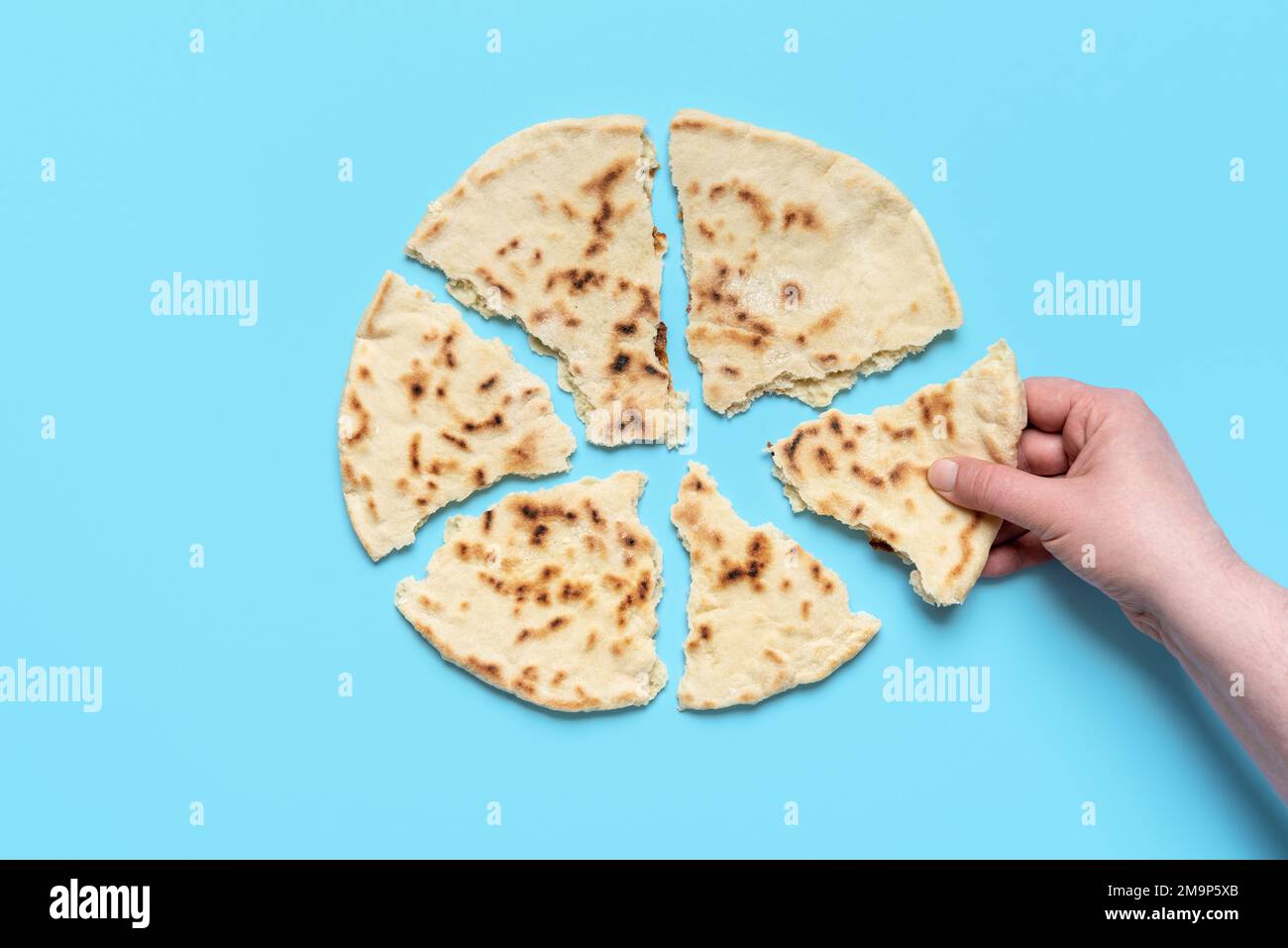 Above view with a woman's hand taking a piece of flatbread, minimalist on a blue table. Homemade