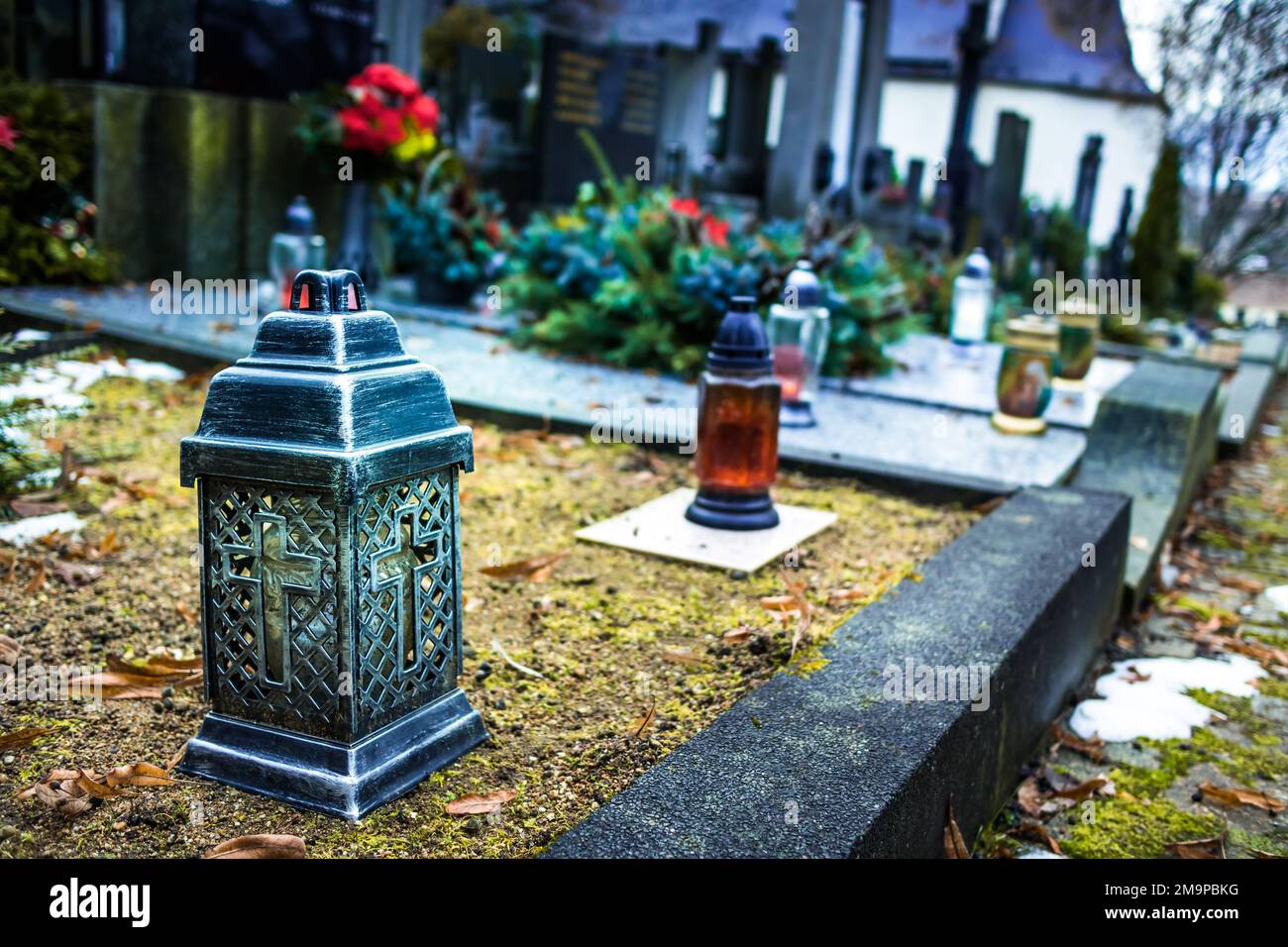 Candle lantern at grave in cemetery. Grief and paying respect for dead person. Tombstones and a chapel in the public cemetery Stock Photo