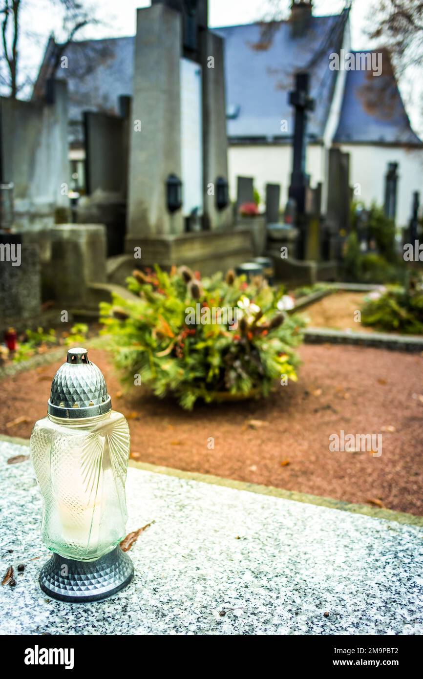 Candle lantern at grave in cemetery. Grief and paying respect for dead person. Tombstones and a chapel in the public cemetery Stock Photo
