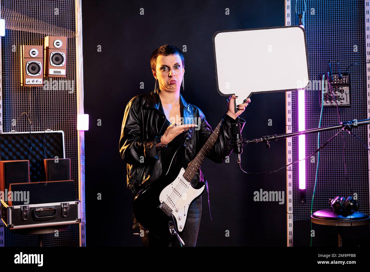 Rocker artist pointing at blank advertising board while playing at electric guitar preparing for rock concert. Musician with grunge style performing heavy metal song in studio, checking instrument sound Stock Photo