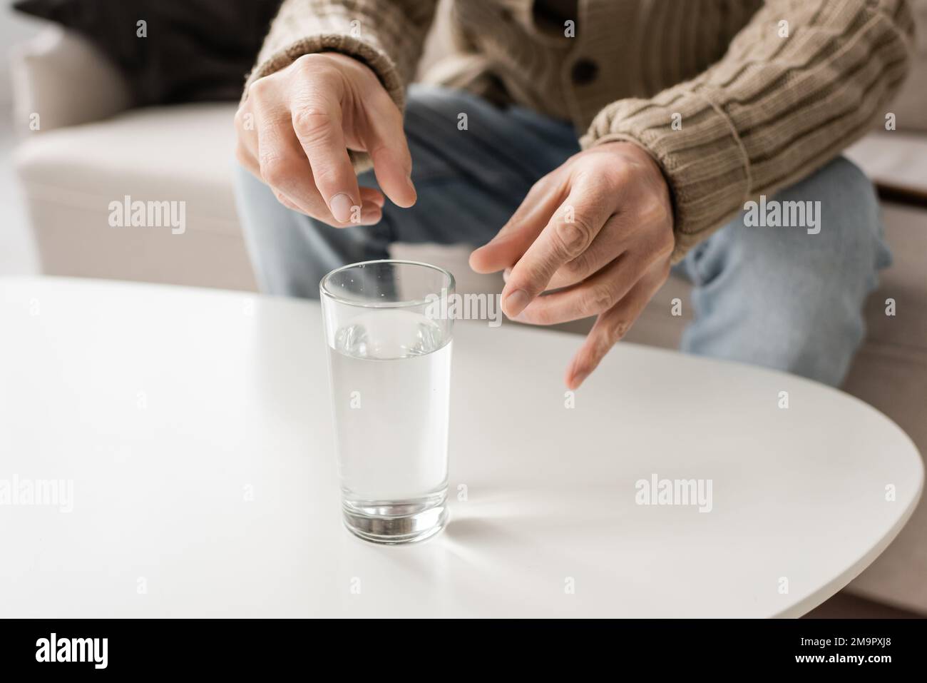 cropped view of man with parkinson disease and trembling hands sitting near glass of water at home,stock image Stock Photo