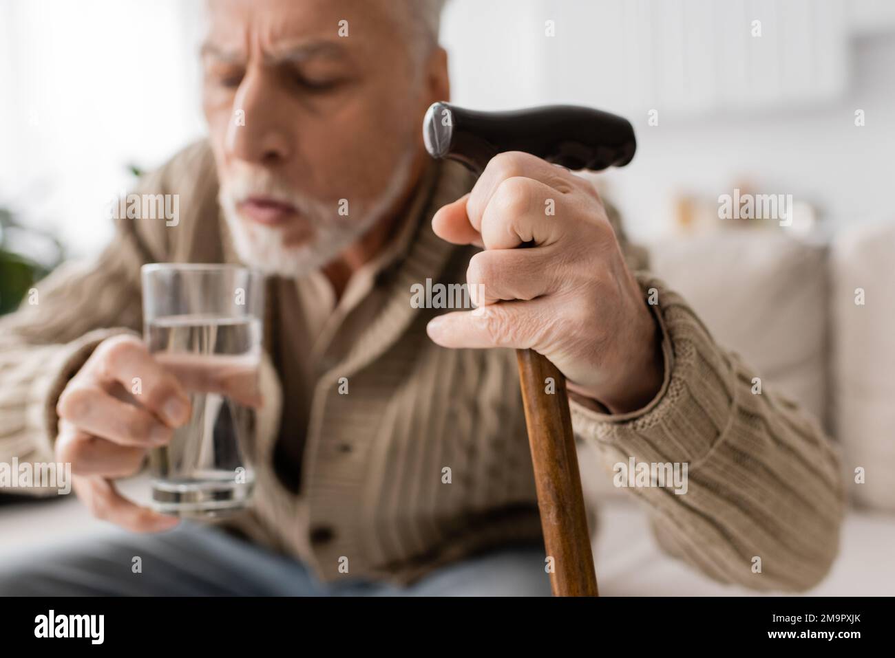 blurred man with parkinsonian syndrome holding walking cane and glass of water in trembling hands,stock image Stock Photo