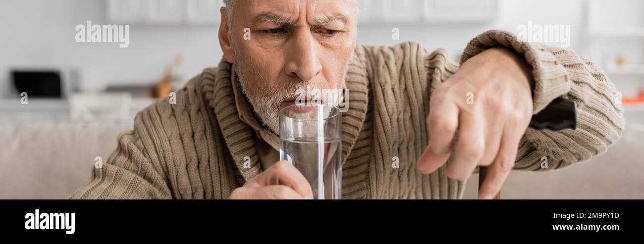 worried man with parkinsonian syndrome holding glass of water in trembling hand, banner,stock image Stock Photo