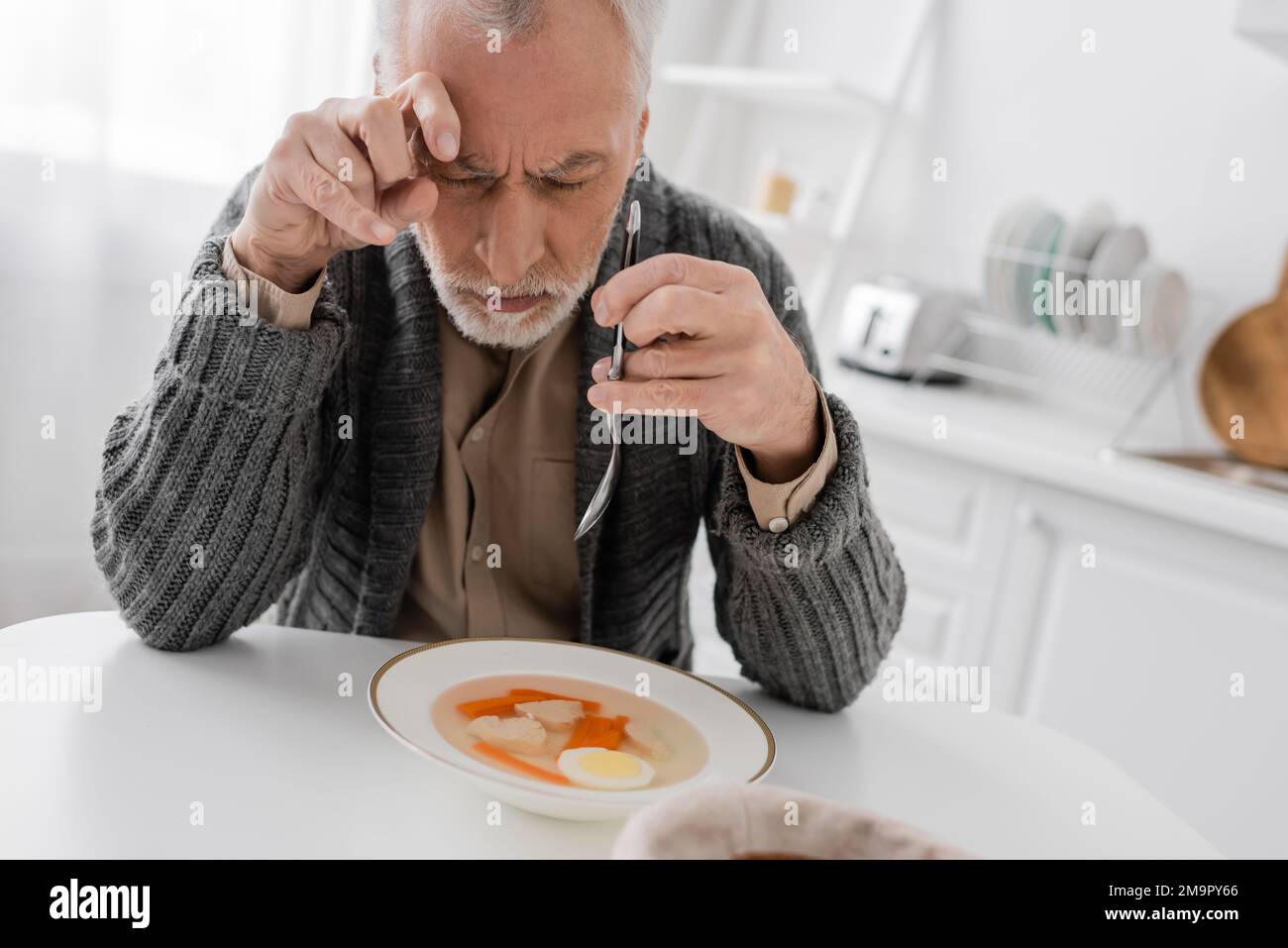 depressed man with parkinson syndrome holding spoon while sitting with