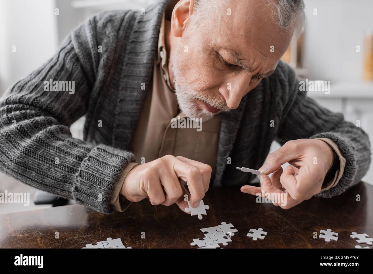 senior man with trembling hands caused by parkinson disease combining jigsaw puzzle at home,stock image Stock Photo
