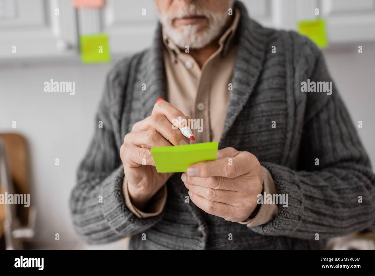 cropped view of aged man with alzheimer disease writing on sticky notes ...