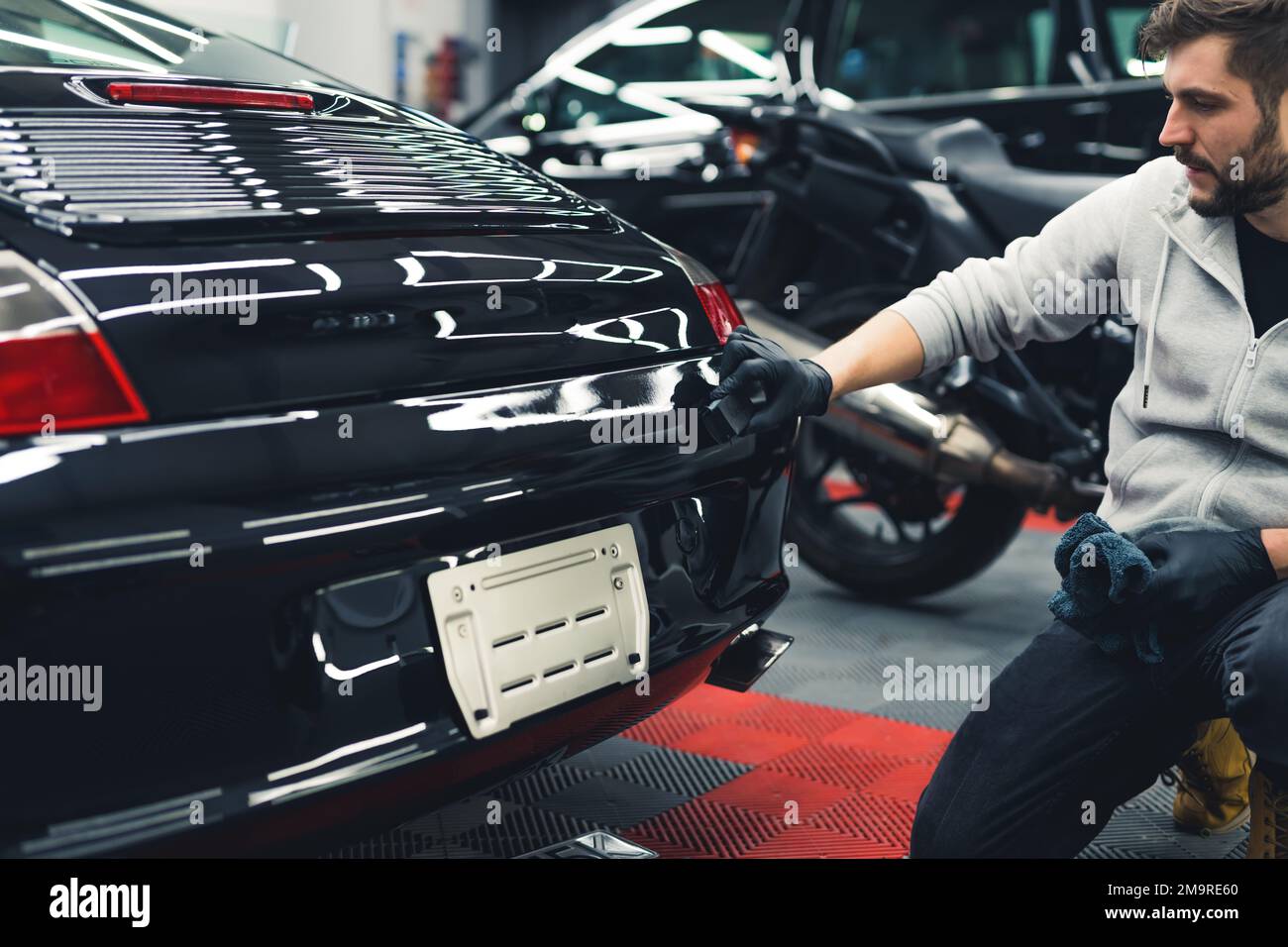 Black car spoiler and back during application process of ceramic coating. Professional male worker doing car detailing with a sponge. High quality photo Stock Photo