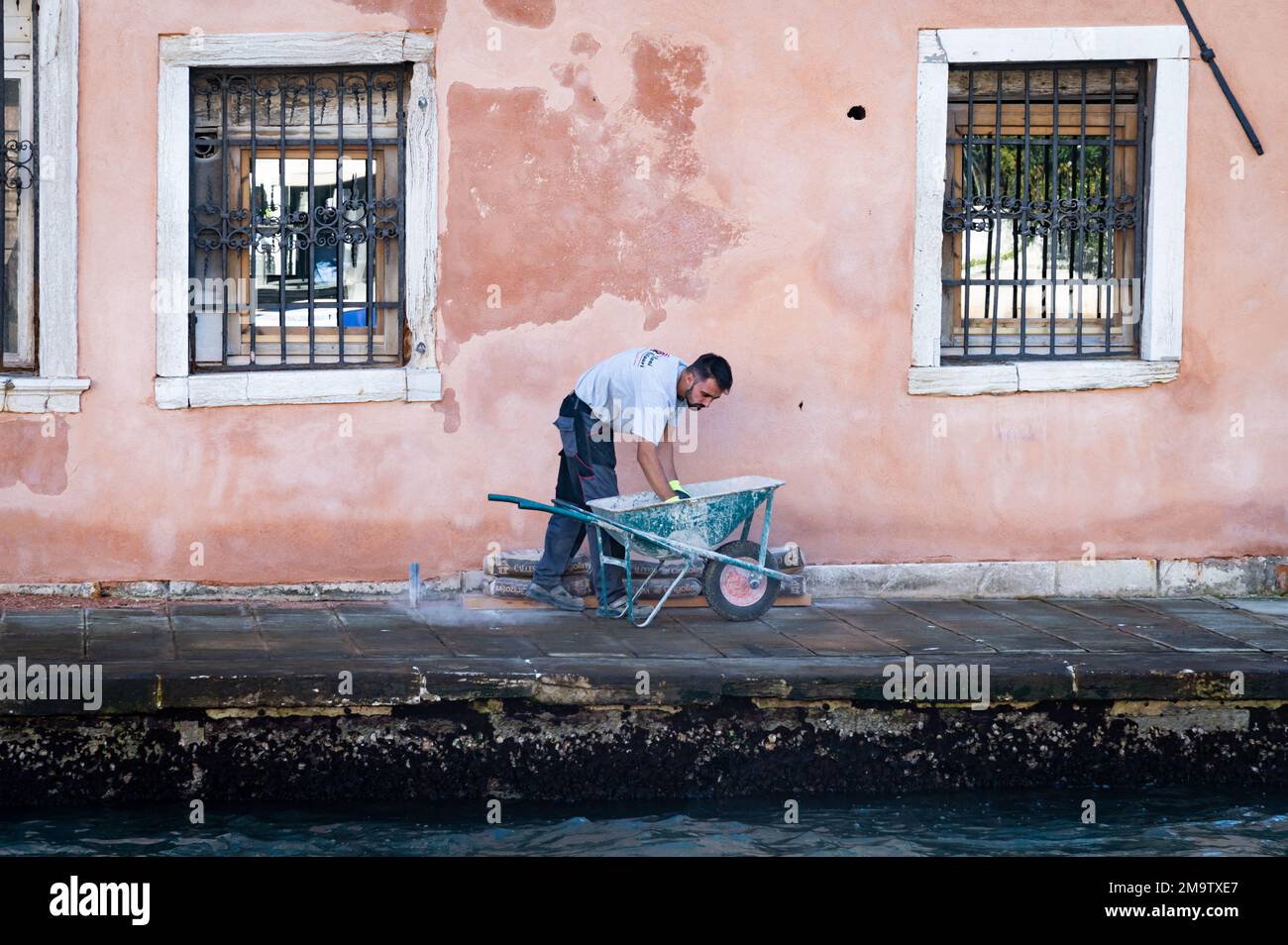 A construction worker works on patching the colorful side of a building in Venice on the Grand Canal. Stock Photo