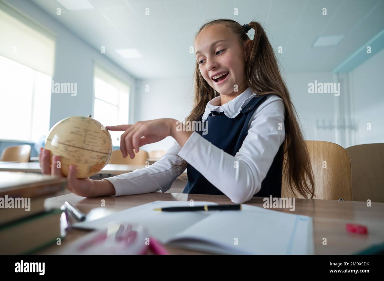 Caucasian schoolgirl sits at her desk at school and studies the globe ...