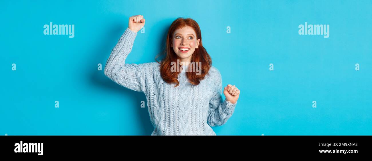 Happy redhead girl rooting for team, cheering with raised hand and ...