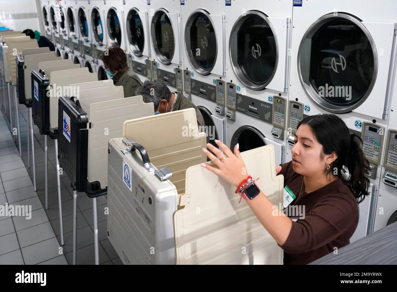 Poll worker Alany Gonzalez sets up another voting booth in front of dryers  at the Su Nueva Lavanderia near Chicago's Midway Airport Tuesday, Nov. 8,  2022, in Chicago. (AP Photo/Charles Rex Arbogast