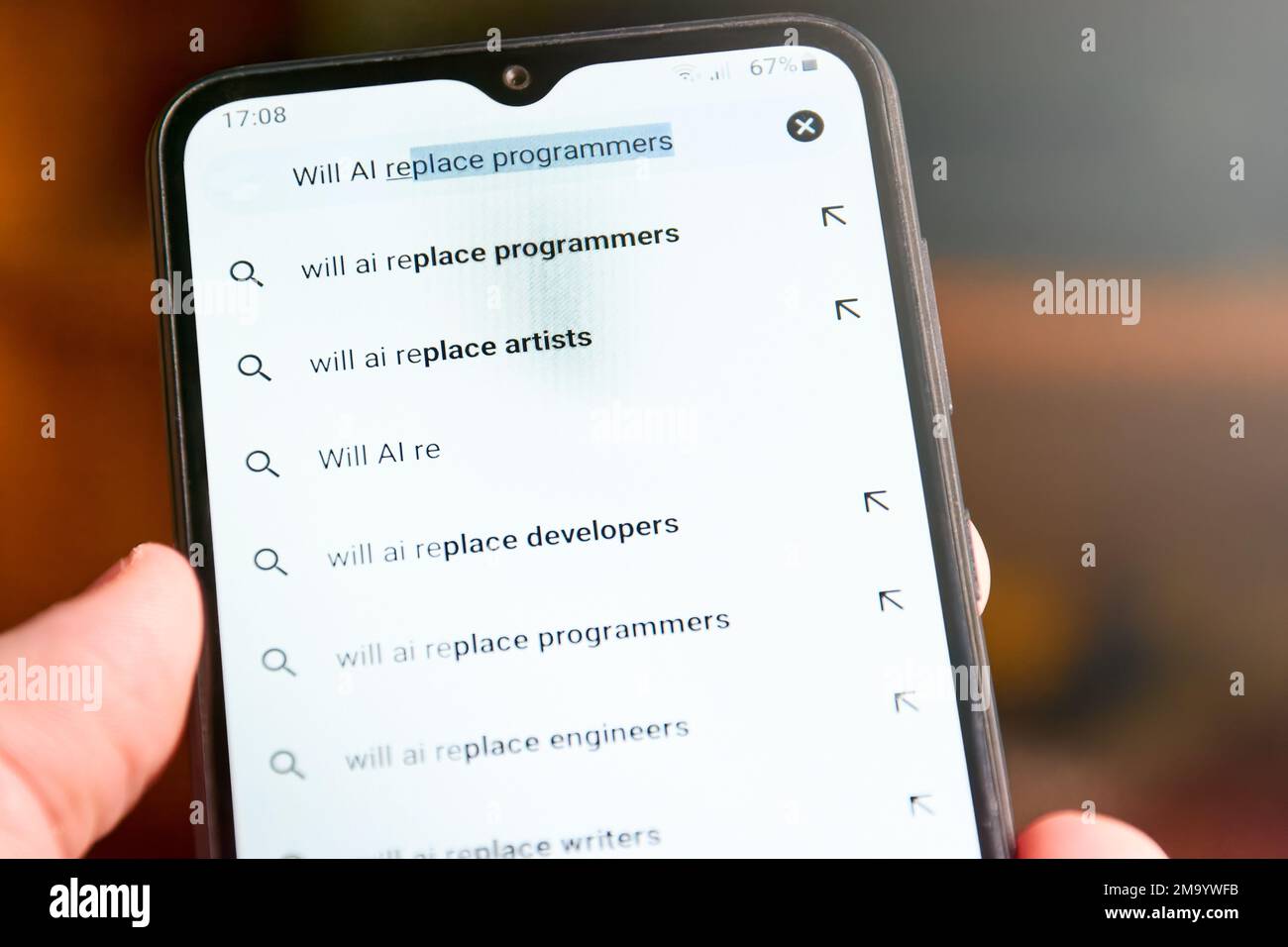 Horizontal close up of mobile phone screen with search 'Will AI replace programmers' and list of suggested searches below. People searches on AI, conc Stock Photo