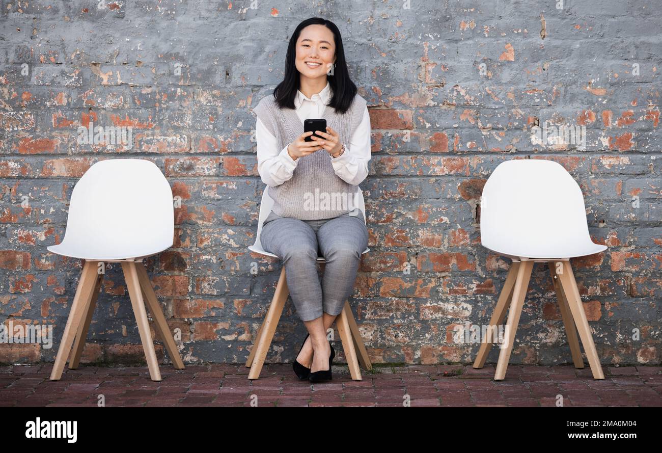 Woman waiting for interview on chair with phone, recruitment and employment with smile. Portrait of happy person in Japan sitting on chair, smiling Stock Photo