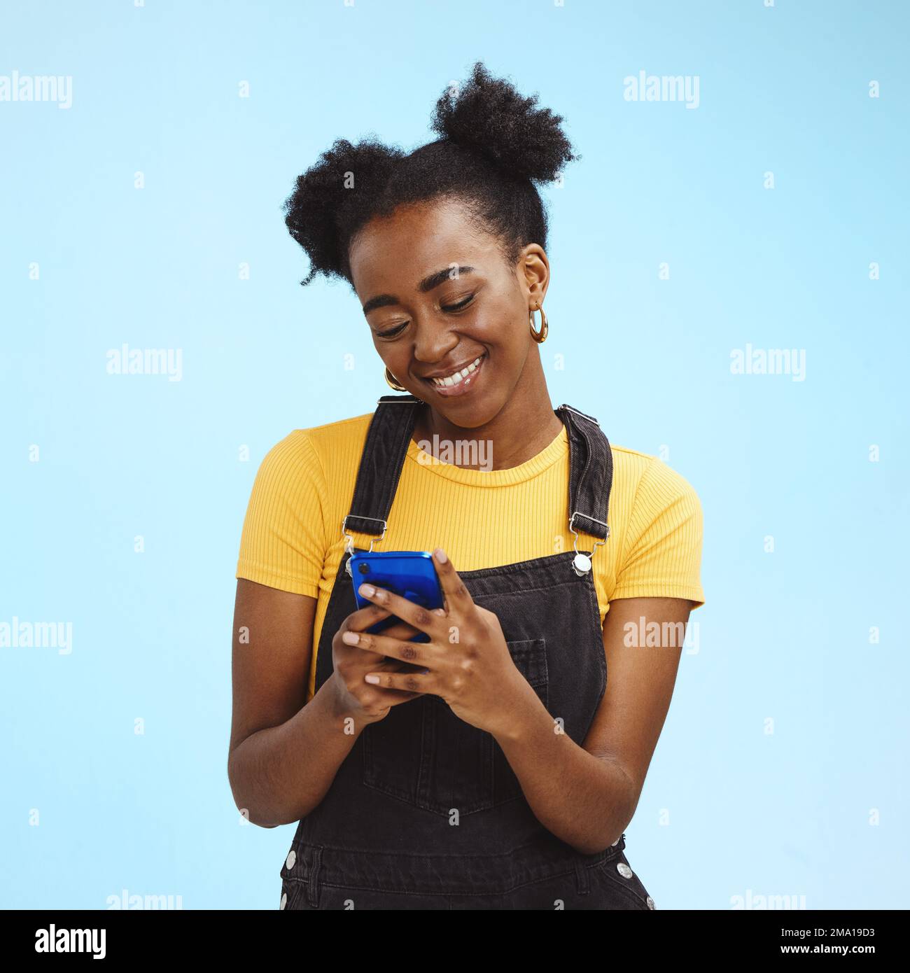 Black woman with smartphone in hands, smile and happy with chat or social media, communication isolated on blue background. Technology, happiness and Stock Photo