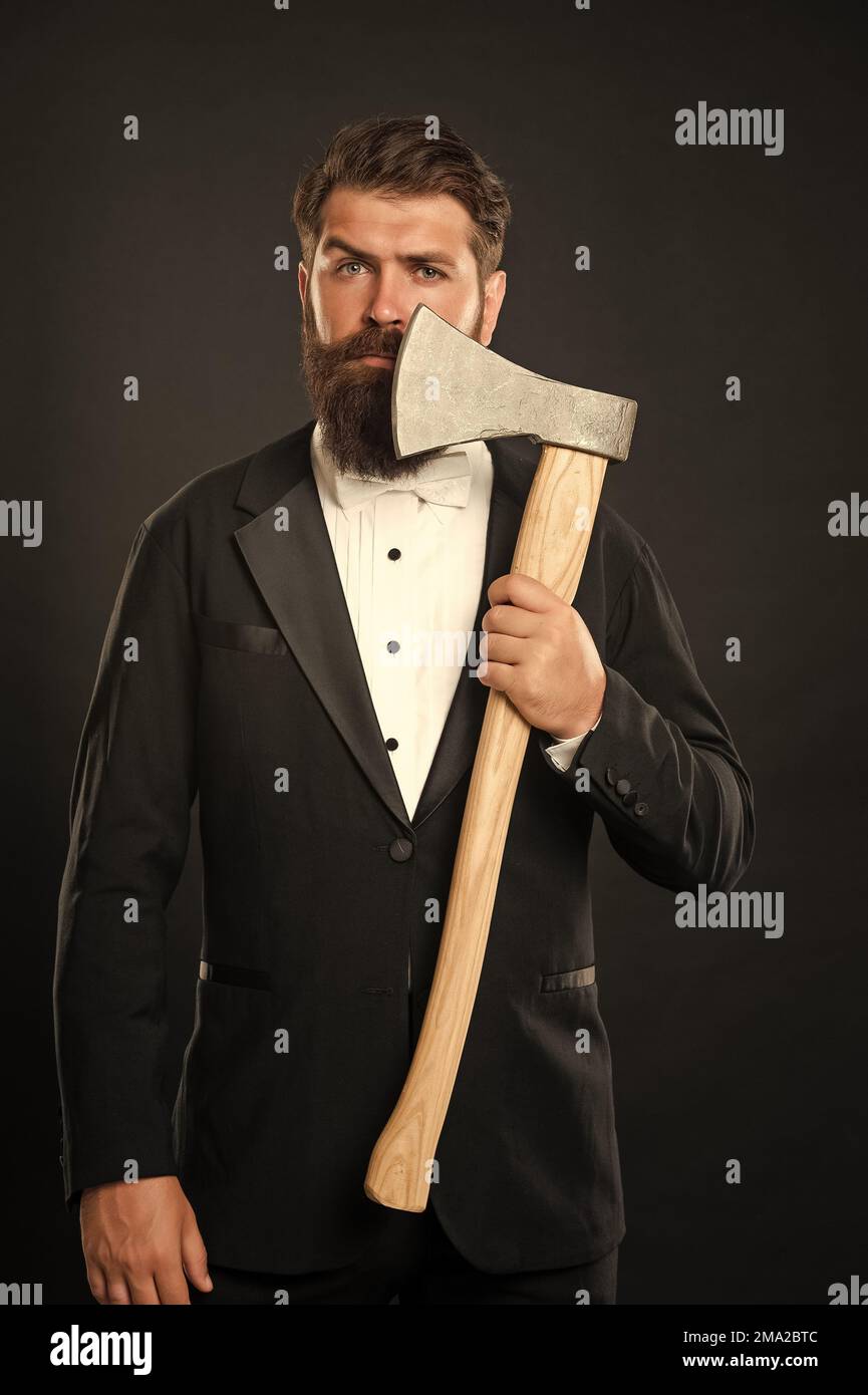 Serious bearded man in formal suit holding hatchet at unshaven face ...