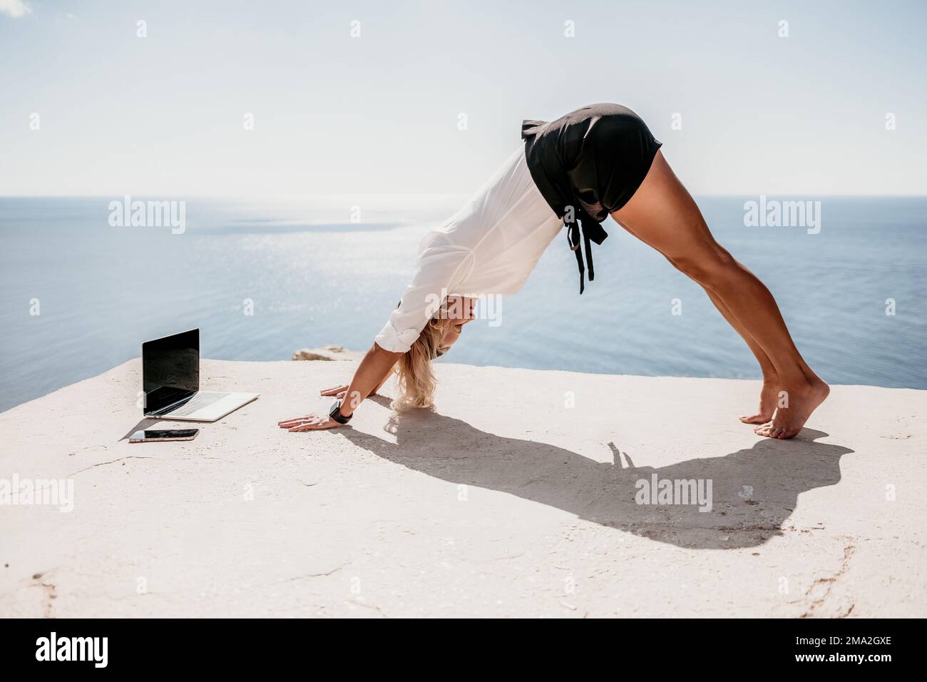 Woman sea laptop yoga. Business woman freelancer in yoga pose working over blue sea beach at laptop and meditates. Girl relieves stress from work Stock Photo