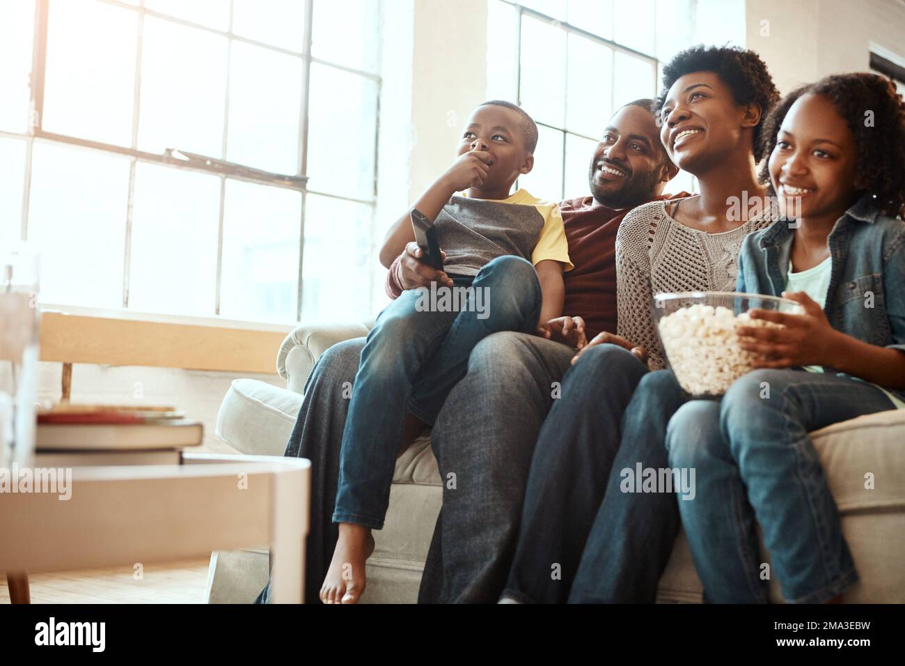 Happy black family on sofa for movie, television or film together, bonding and quality time in living room. Popcorn, kids TV show and people, mother Stock Photo